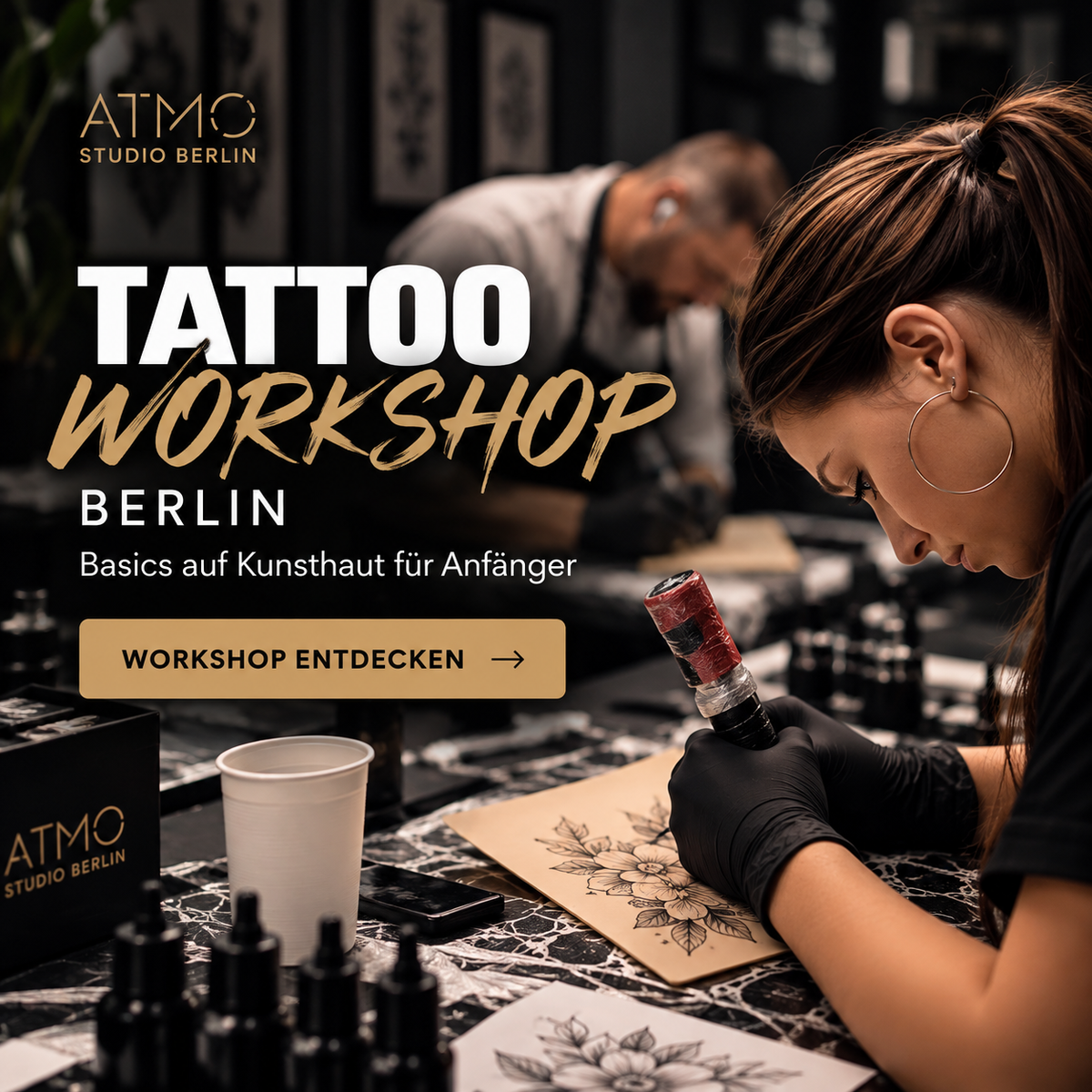 Promotional graphic for an ATMO Studio Berlin Tattoo Workshop, showing a woman in a tattoo studio wearing black gloves and applying a floral tattoo on skin with a tattoo machine. Large German text reads 'TATTOO WORKSHOP BERLIN' and 'Basics auf Kunsthaut an Anfänger'.